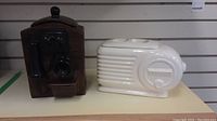 Two ceramic cookie jars on display: a dark brown antique telephone and a white vintage radio.