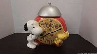 Front view showing Snoopy and Woodstock on cookie-themed jar with silver lid on.