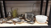 Photo showing the full collection of vintage kitchen items on shelf, including metal meat grinders, glass pitcher, electric toaster, Simple Cooker bowl, metal cocktail shaker, wire egg holder, and utensils.