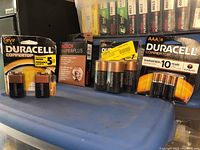 Various Duracell Coppertop batteries in sealed blister packs and loose, alongside a Bosch Super Plus 4-pack of spark plugs on a blue plastic container.