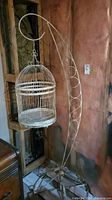 Full view of metal bird cage hanging from curved metal stand showing overall height and structure