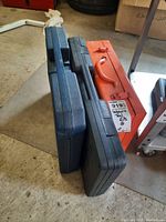 Three closed tool cases: black plastic case, black plastic case, orange metal case for the Ramsey D60