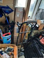 View of black metal utility cart with handle and wheels stored upright next to window with other items