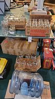 Photo showing multiple Bernardin Mason jars in original box and additional jars with metal lids on a glass table, with a large clear water bottle with a spigot standing in front.