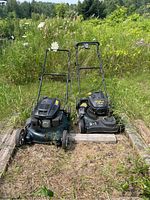 Two Yard Works push lawnmowers positioned side by side outdoors with vegetation in background.