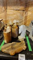 Photo showing six onyx goblets, fish-shaped ashtray, and horse head figurine grouped together on table with background wall.