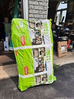 Full view of sealed Keter resin outdoor storage unit package standing upright outside a garage.