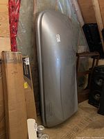 Side angle view of silver SportRack roof cargo box leaning against wall