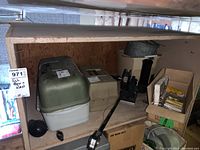 Shelf with two plastic fishing tackle boxes, fishing reels mounted on rod holder, buckets, and boxes with fishing accessories