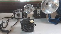 Three vintage Brownie cameras displayed together. The Baby Brownie Special in front, with Brownie Hawkeye and Brownie Holiday Flash behind, both equipped with large flash reflectors.