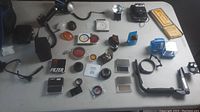 Wide view of miscellaneous camera accessories on a table showing flashes, filters, lens attachments, and other camera-related items.