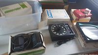 Overview photo showing multiple items including Kodak Carousel trays, boxes of blank slides, Omega Pro-Lab timer, metal tray, and wave-wash agitator on a table.