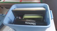 Blue storage tub containing green and yellow photo development trays along with other items including a black cylindrical container labeled 'Clarityrome'