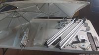Three Reflectasol umbrellas, two aluminum stands, several metal brackets, and hardware laid out on table