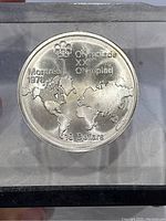 Obverse side of Canadian silver coin with Montreal 1976 Olympics logo, world map, and denomination.