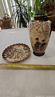 Photo of both antique Asian pieces on a white surface with a yellow measuring tape showing size.