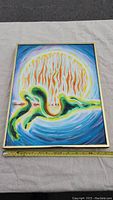 Front of framed painting laid flat on fabric background with measuring tape showing approx. 28″ width.