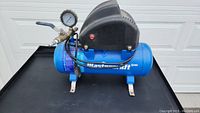 Front view of Mastercraft blue 2 gallon air compressor with motor cover and pressure gauge attached