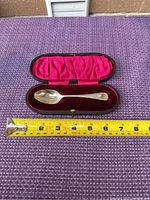 Sterling silver spoon in fitted case with red velvet and satin lining and measuring tape indicating length around 4.5 inches.