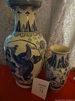 Pair of two blue and white porcelain Asian vases with detailed designs against a patterned background and red surface