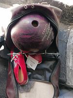 Purple Brunswick bowling ball with red bowling shoes and black carrying bag.