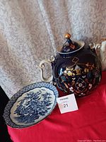 Photo shows blue and white floral ceramic plate next to dark blue floral and gold ceramic teapot with ivory handle and lid.