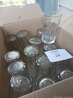 Box of small plain drinking glasses upside down, showing mostly bottoms and one tall Bud glass upright.