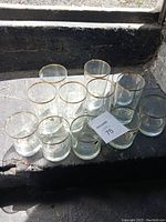 Top view of eleven small clear glasses arranged neatly on a dark surface, each showing a gold band at the rim.