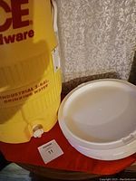 Side view of yellow 5-gallon industrial drinking water jug and stack of white paper plates on a table.