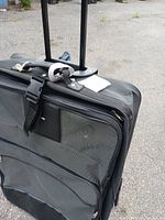 Overall view of gray and black suitcase with zippered compartments and extendable trolley handle in upright position.