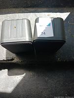Photo showing the backs of two small speakers, silver-gray with ridged design and connection points.
