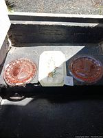 Three trays arranged on an outdoor concrete surface. Two round pink glass trays and one rectangular white ceramic egg tray with floral artwork.