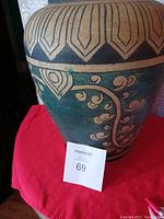 Photo of large, heavy brass vase showing detailed floral and geometric engraved decorations on its body with green and black coloring.
