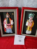 Two framed relief block art pieces, one male character with long beard and pink robe, one female character with intricate headdress and yellow robe, both in red frames.
