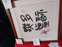 Front view of the framed Chinese or Asian calligraphy wall art with visible red stamps and brown wood frame.