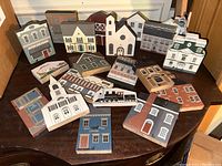Photo showing full assortment of 20 wooden Cats Meow village buildings on a wooden table. Buildings represent various houses, churches, barns and commercial storefronts with painted details.