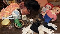View of various vintage dolls, gloves, decorative items including green dragon figurine, white gloves, black gloves, ceramic pieces, and hats.