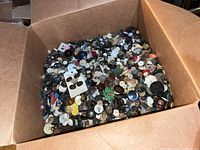 Photo of the large open cardboard box three-quarters full of mixed buttons of many styles and colors.