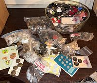 Top-down image of assorted large buttons in plastic bags and loose in a bowl on a surface.