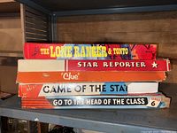 Stack of six vintage board games on a shelf showing titles, colors, and box conditions.