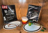 View of the lot including Life magazine, Post magazine, Tupperware bowls, macrame owl hanging, Pyrex platters, and a yellow handled spoon.