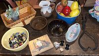 Photo of the lot including three stoneware bowls, assorted artificial fruit, vintage metal tongs, a floral porcelain dish, a bowl with buttons, small figurines, and a wooden tile with violin painting.