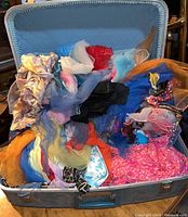 Vintage blue suitcase open showing a colorful assortment of vintage scarves and a wedding veil inside.