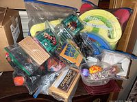 Top-down view of assorted toys and games packed in resealable plastic bags and loose, showing edges of crates and labels