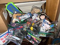 Overview of assorted toys including a cloth doll, toy figurines, puzzle pieces, and other small items in clear plastic bags.
