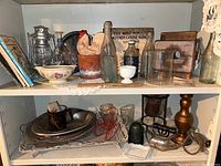 Two shelves of assorted vintage decor items, kitchenware, books, bottles, and collectibles displayed inside a white shelving unit.