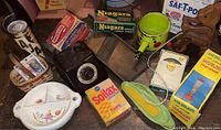 Photo showing a collection of vintage advertising boxes, child serving dish with colorful illustrations, button packages, nickel plated scale, wooden dog figurine, toy corn on the cob, and various other vintage kitchen and collectible items.