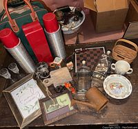 Photo of all lot items arranged on a wooden table including thermoses, dishware, glassware, framed art, and wooden decor