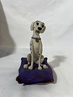 Front view of the Perdita sculpture seated on a purple cushion showing detailed spots and facial expression.