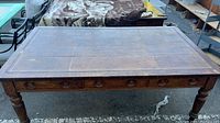Full view of the large rectangular wood table with leather inlay on top, showing wear and surface damage.